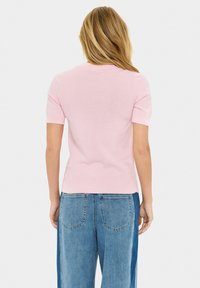 Maglione corto a maniche corte di colore rosa chiaro con un design attillato, colletto e orlo a costine. Abbinato a jeans in denim blu a vita alta.