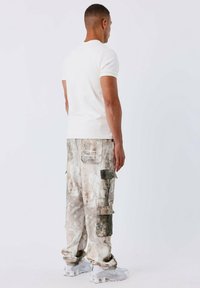 Witte kortemouw t-shirt gecombineerd met gestreepte cargobroek in beige en grijs, met meerdere zakken, en witte sportschoenen.