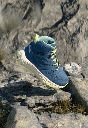 Niebiesko-szare buty trekkingowe z siateczkową cholewką, żółtymi akcentami i wytrzymałą podeszwą, uniesione nad skalistym terenem. Posiadają wyściełany kołnierz.