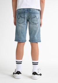 Shorts di denim azzurri chiari con taglio dritto, orli arrotolati e due tasche posteriori con cuciture decorative. Abbinati a calze bianche e sneakers nere.