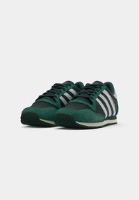 Green and black sneakers with suede and synthetic materials, featuring three white stripes, a rounded toe, and textured rubber outsole.