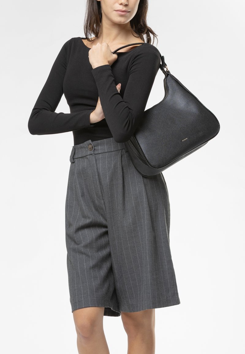 Borsa a tracolla in pelle nera con una texture liscia, forma curva e chiusura con zip, abbinata a pantaloni corti a vita alta con righe grigie.