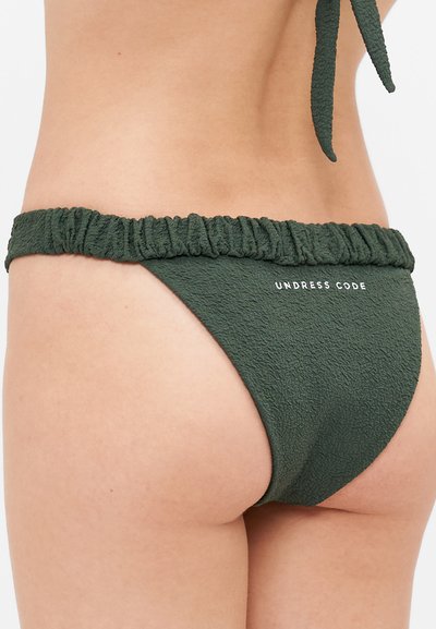 Zaļas teksturētas bikini apakšdaļa ar elastīgu ruffles jostasvietu un logo detaļu. Audums izskatās mīksts un stiepjams.