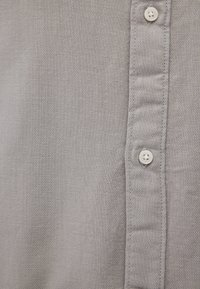 Gray button-up shirt with a smooth texture, featuring a vertical row of white buttons and plain stitching along the placket.