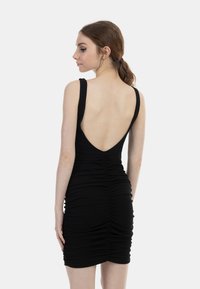 Rochie neagră tip bodycon din material încrețit, cu un decolteu adânc pe spate, bretele groase și detalii strânse pe părți pentru o siluetă care se mulează pe corp.
