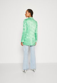 Blazer verde texturat cu un model de dungi de tigru, purtat cu blugi evazați de culoare albastru deschis și pantofi cu toc metalici.