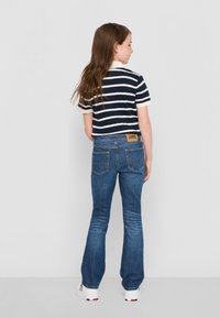 Polo à manches courtes rayé bleu marine et blanc associé à un jean évasé bleu. Le jean présente une patch marron avec une marque et deux poches arrière.