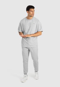 T-shirt grigio in cotone a maniche corte e pantaloni della tuta coordinati con una vestibilità comoda. Dettagli notevoli includono un piccolo logo e caviglie arrotondate.