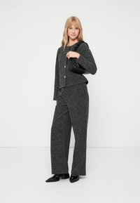 Γκρι υφασμάτινη πλεκτή ζακέτα με κουμπιά, σε συνδυασμό με παντελόνι φαρδύ που ταιριάζει. Συμπληρώνεται με μια μικρή μαύρη τσάντα και μαύρες επίπεδες παπούτσια.