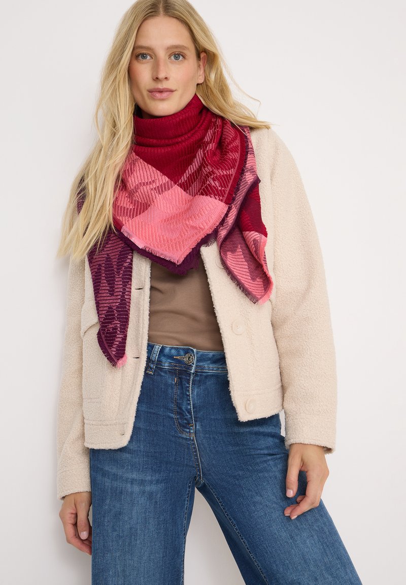 Rød og pink plaid tørklæde med tekstureret finish, draperet om halsen. En hyggelig cremefarvet jakke, brun top og blå jeans fuldender outfittet.