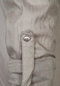 Polsino di camicia in lino grigio chiaro con bottone d'argento e dettaglio con patta cucita. Il tessuto ha una finitura morbida e testurizzata.