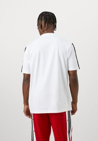 Hvit bomulls t-skjorte med korte ermer, med svarte aksentstriper på skuldrene og en avslappet, rettskåret design.