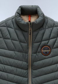 Gepolsterte graue Jacke mit hohem Kragen, ausgestattet mit einem Reißverschluss, beige Innenfutter und einem orangefarbenen Akzent-Logo auf der linken Seite.