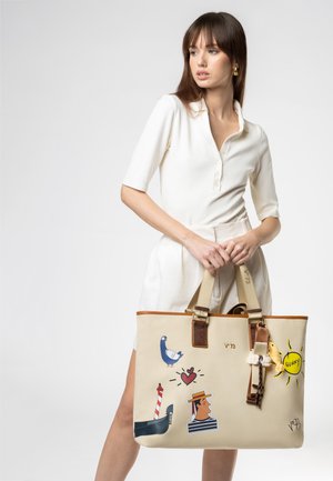 Donna in abito bianco che tiene una borsa tote beige con stampe colorate in stile cartone animato, inclusi un piccione, un cuore, un faro, un volto maschile e un sole con la scritta "sunny".