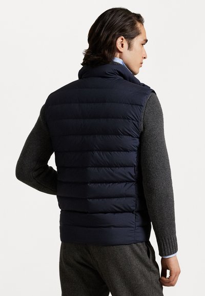 Navy blue puffer vest with quilted design, high collar, and zip closure. Worn over a gray sweater, showcasing a textured finish.