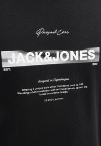 Sort bomulds t-shirt med hvid tekst: "JACK&JONES," "Project Core," og designdetaljer, med en blød tekstur og moderne typografi.