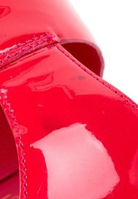 Gros plan d'une chaussure en cuir verni rouge brillant avec des coutures visibles et une ouverture incurvée.