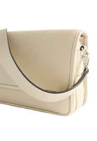 Beżowa skórzana torebka o teksturowym wykończeniu, z ciemnym akcentem na pasku oraz eleganckim, prostokątnym designie z zaokrąglonymi krawędziami.