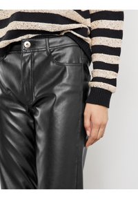 Zwarte faux leren broek met een gladde textuur, voorzien van zijzakken en een zichtbare knoopsluiting. Draagbaar met een gestreepte trui.