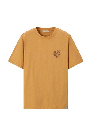 T-shirt jaune moutarde à manches courtes avec col rond et petit motif graphique sombre de feuilles et texte sur la poitrine gauche.