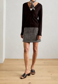 Svart cardigan med v-ringning och knappar, kombinerad med en mönstrad svartvit minikjol. Svarta läderklacksklackar. Scarff accent.