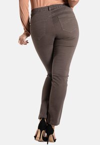 Pantalon en denim marron avec une coupe slim, doté de poches arrière et de coutures détaillées, associé à des chaussures à talons hauts noires.