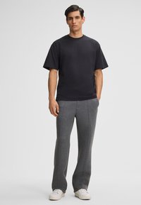 Zwarte katoenen t-shirt met een ronde hals, gecombineerd met grijze, gestructureerde joggers met zijnaadaccenten en witte sneakers.