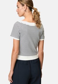 Striped short-sleeve top in white and navy, featuring a crew neckline and ribbed texture, paired with navy trousers.