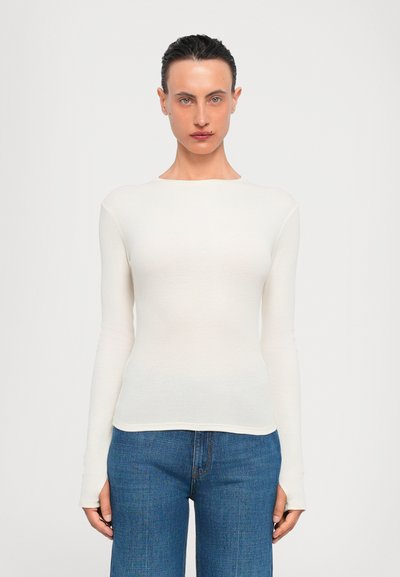 Blusa blanca de manga larga, ligera, con escote redondo, diseño ajustado y una textura sutil; combinada con jeans azul de pierna recta.