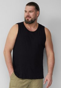 Schwarzes ärmelloses Tanktop aus leichtem Stoff, mit rundem Halsausschnitt und lässiger Passform, kombiniert mit beigen Shorts.