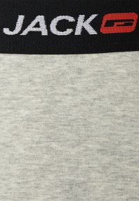 Hellgrauer Stoff mit feiner Textur, der einen breiten schwarzen Bund mit weißen und roten "JACK"-Text und Logo aufgedruckt hat.
