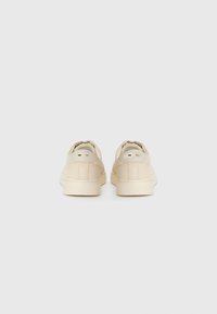 Beige suede sneakers with a smooth texture, featuring a low-top design, rounded toe, and minimalistic accents on the heel.