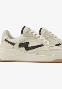 Cream leather sneakers with black embroidered accents, textured heel, and white laces. Rubber sole adds stability and grip.