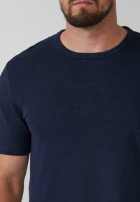Marineblauwe T-shirt met korte mouwen van een textuurstof, met een ronde halslijn en subtiele stikseldetails bij de hals en zijkant.