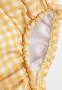 Tessuto a quadri giallo con check bianchi, dotato di bordo elastico arricciato e morbida fodera interna, che presenta una texture liscia e un colore vivace.