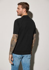 Svart polo med korta ärmar, texturerad tyg och krage. Tillsammans med ljusblå denimjeans, med bakfickor.