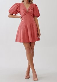 Krátké rukávy, korálová šaty s hlubokým výstřihem ve tvaru V a zúženým pasem. Obsahuje kulatou akcentaci a plisovanou sukni, vyrobenou z hladkého materiálu.