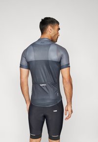 Tricou de ciclism cu mânecă scurtă în gri închis, cu panouri din plasă pentru respirabilitate, asociat cu pantaloni scurți de ciclism negri, cu accente reflective.