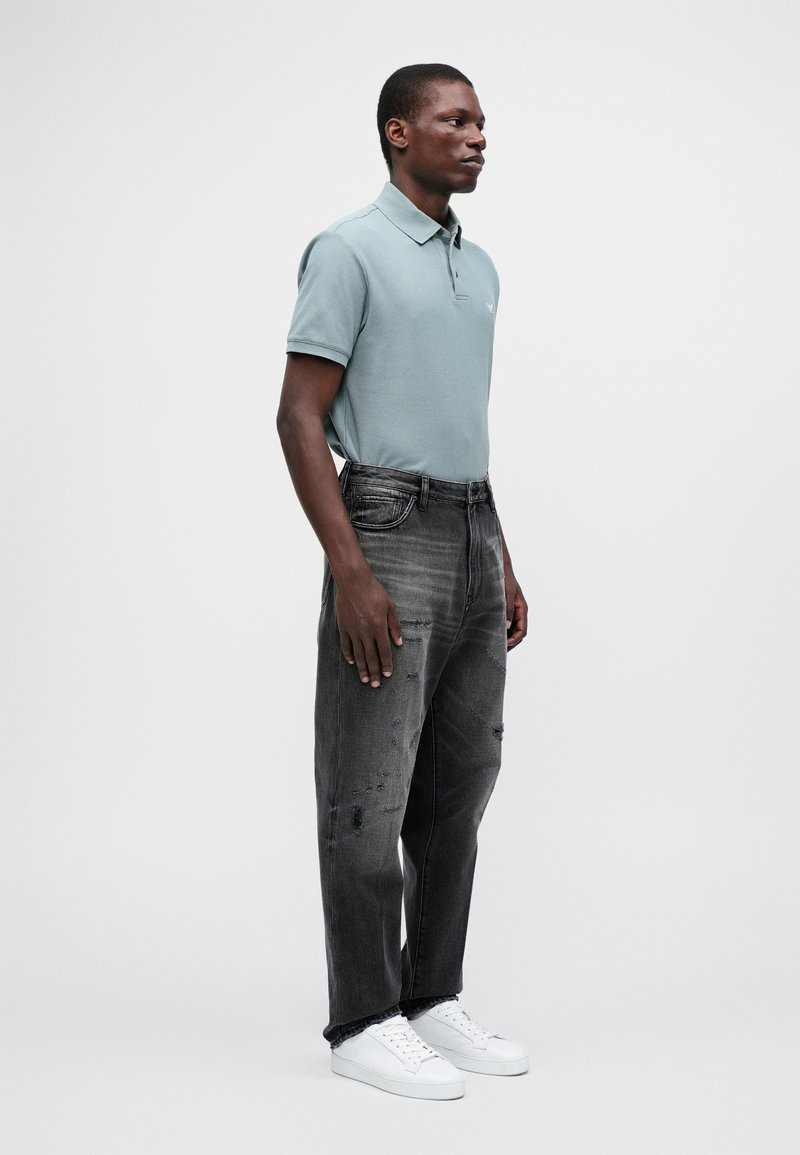 Polo bleu clair avec un col classique, associé à un jean noir déchiré et des baskets blanches. Design simple et moderne.