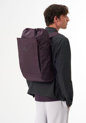 Lila Rucksack mit einem Kordelzug oben und einer Reißverschlusstasche vorne. Hergestellt aus strapazierfähigem Material, mit zwei schwarzen Punkten als Akzenten.