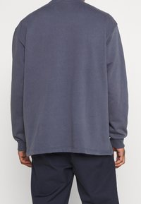 Sudadera de algodón gris oscuro de mangas largas y cuello redondo. Presenta un ajuste relajado, puños acanalados y un dobladillo recto con un detalle mínimo.
