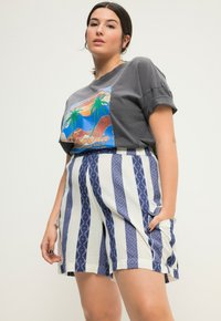 Šedé tričko s barevným grafickým designem, doplněné o šortky s vysokým pasem a vzorem, které mají modré pruhy a geometrické tvary.