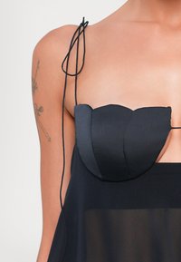 Vestido negro de corte off-the-shoulder con material satinado, corsé estructurado en la parte superior, tirantes ajustables y panel inferior transparente.