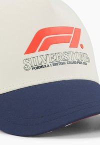 Biała czapka baseballowa z granatowym daszkiem. Na przodzie znajduje się czerwone logo "F1" oraz napis "Silverstone Formula 1 British Grand Prix 2023".