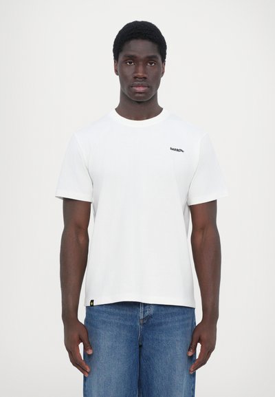 T-shirt en coton blanc avec des manches courtes et un col rond, présentant un petit logo noir sur la poitrine gauche et une étiquette jaune à l'ourlet.