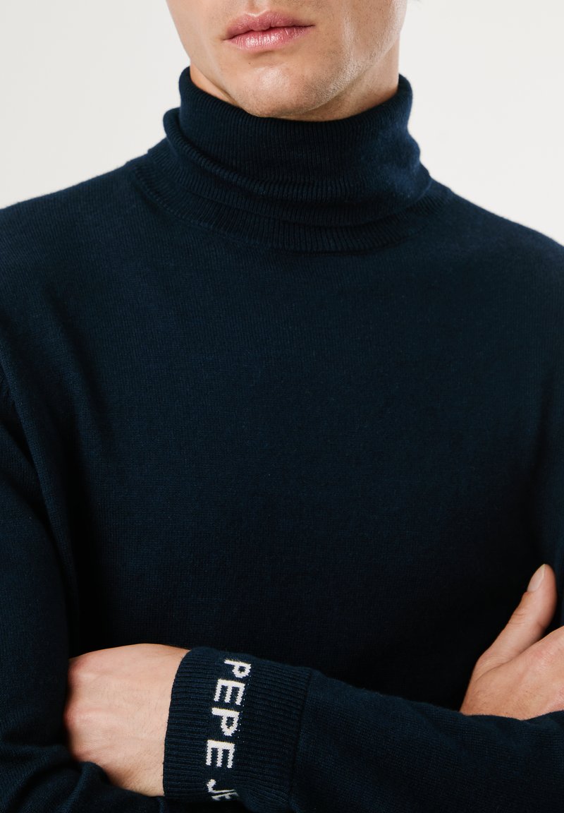 Granatowy sweter z golfem wykonany z miękkiej dzianiny, z prążkowanym wykończeniem przy kołnierzu i mankietach oraz białym logo "PEPE".