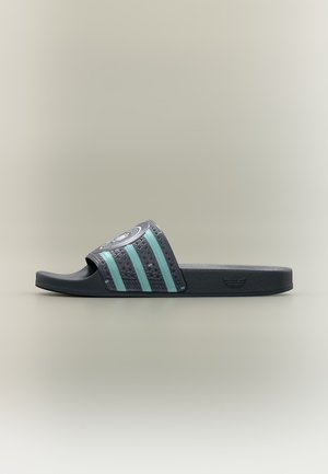 Vue latérale d'une sandale slide noire avec des rayures bleu clair texturées et un logo circulaire sur la bride, présentée sur un fond neutre.