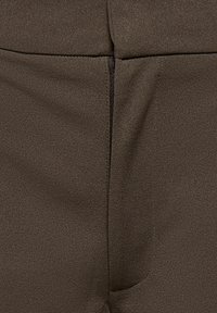 Gros plan d'un tissu brun foncé avec une couture verticale et une texture subtile, montrant des coutures détaillées et de légers plis dans le tissu.