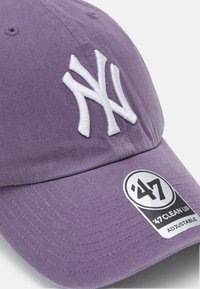 Lilla bomullsbaseballcap med hvit brodert NY-logo. Har en justerbar stropp og et merke på visiret. Teksturert stoff.