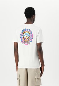 White cotton t-shirt featuring a colorful graphic print on the back, with a smiling cartoon character and bold text elements in blue and pink.
